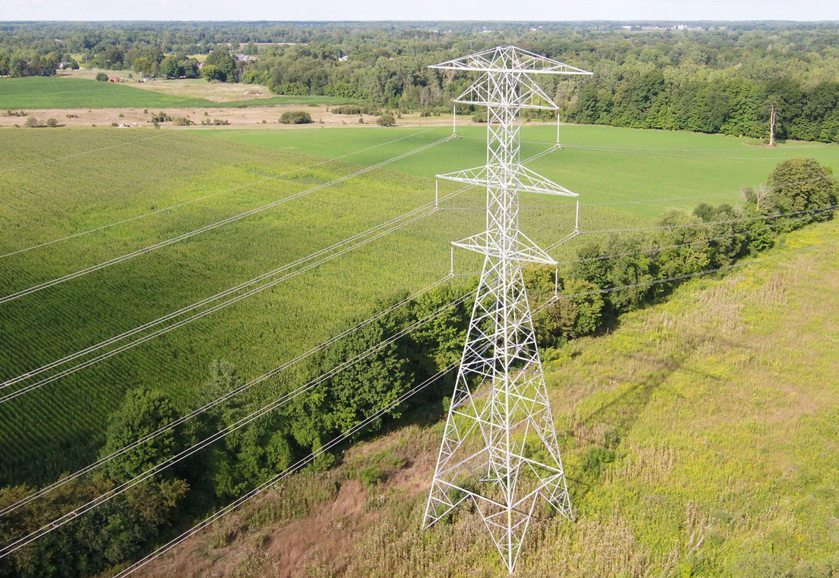 Drone flying in the sky over a power lines above a green field.